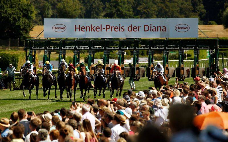 Mehrere Jockeys und Zuschauer beim Henkel-Renntag auf der Galopprennbahn.