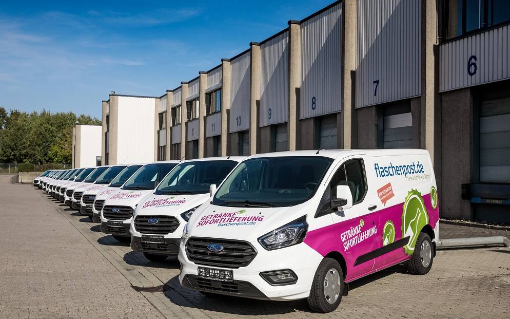 Mehrere Flaschenpost-Transporter stehen vor einer Halle.