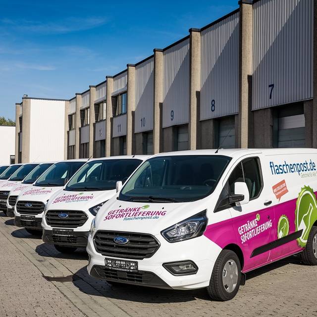 Mehrere Flaschenpost-Transporter stehen vor einer Halle.