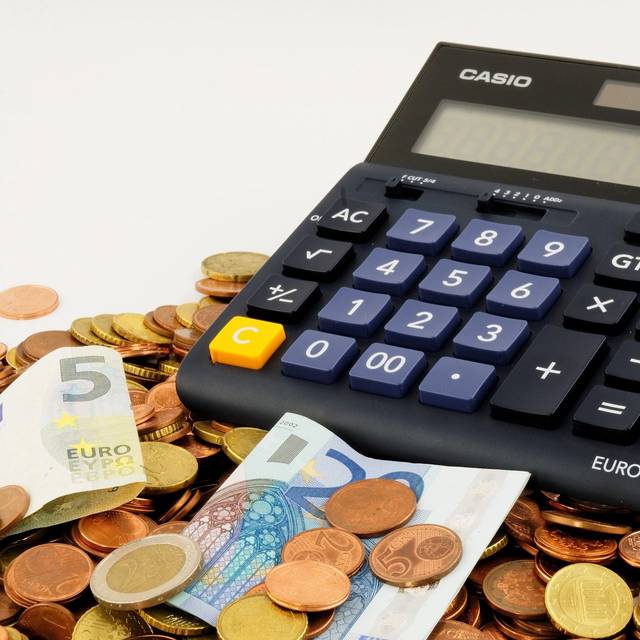 Ein Taschenrechner steht auf Münzen und Euro-Scheinen.