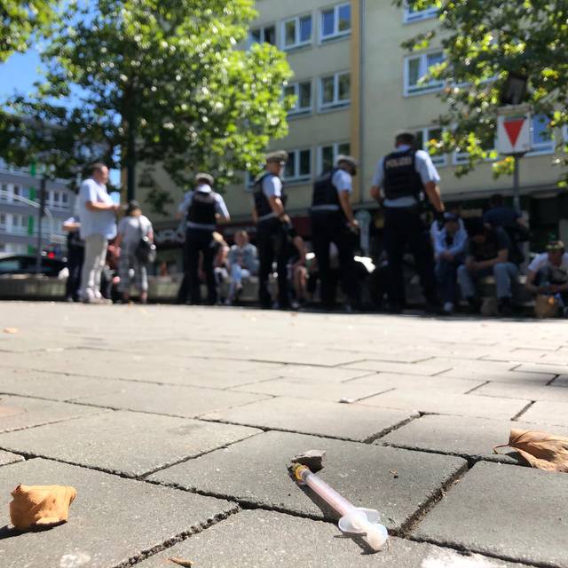 Polizisten im Einsatz auf dem Worringer Platz. Sie kontrollieren Personen, die auf Bänken sitzen.