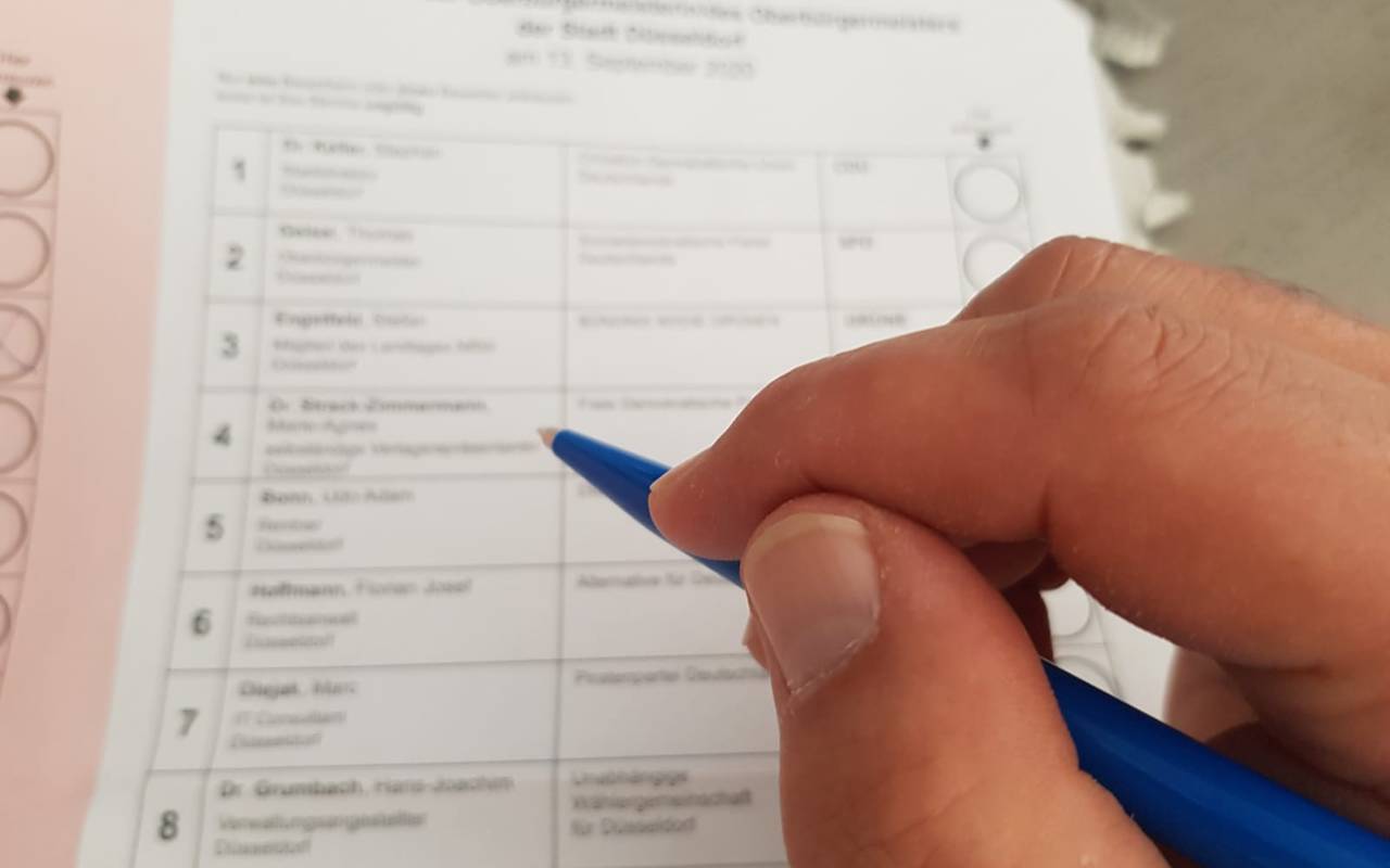 Eine Person hält einen Bleistift in der Hand und macht gleich ein Kreuzchen auf einem Wahlzettel.