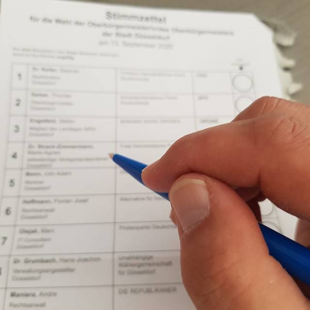 Eine Person hält einen Bleistift in der Hand und macht gleich ein Kreuzchen auf einem Wahlzettel.