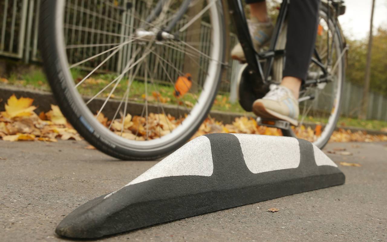 Zu sehen ist aus der Froschperspektive eine Person, die auf einem Fahrrad vorbeifährt. Am Straßenrand liegt Herbstlaub.