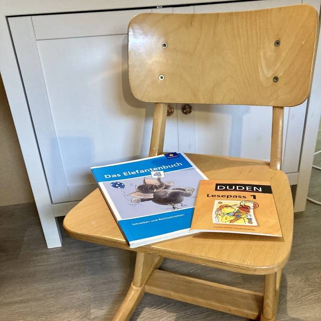 Zwei Schulbücher liegen zum Lernen auf einem Holzstuhl