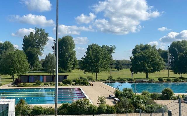 Freibad bei Sonnenschein und einer Wiese im Hintergrund.