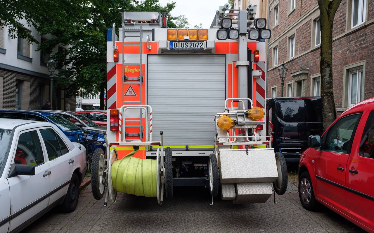 Die Rückseite eines großen Feuerwehrwagens. Links und rechts stehen Wagen. Der Feuerwehrwagen hat Schwierigkeiten, durchzukommen.