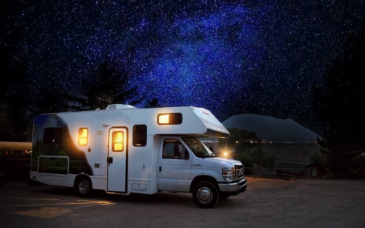 Ein Camper, bzw. Reisemobil steht beleuchtet auf einem Campingplatz. Es ist dunkel.