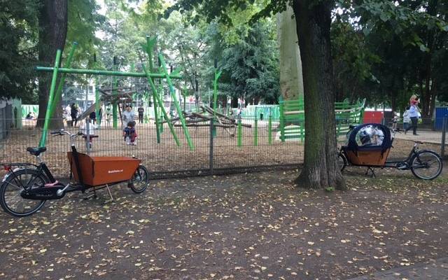 Lastenräder stehen vor einem Spielplatz.