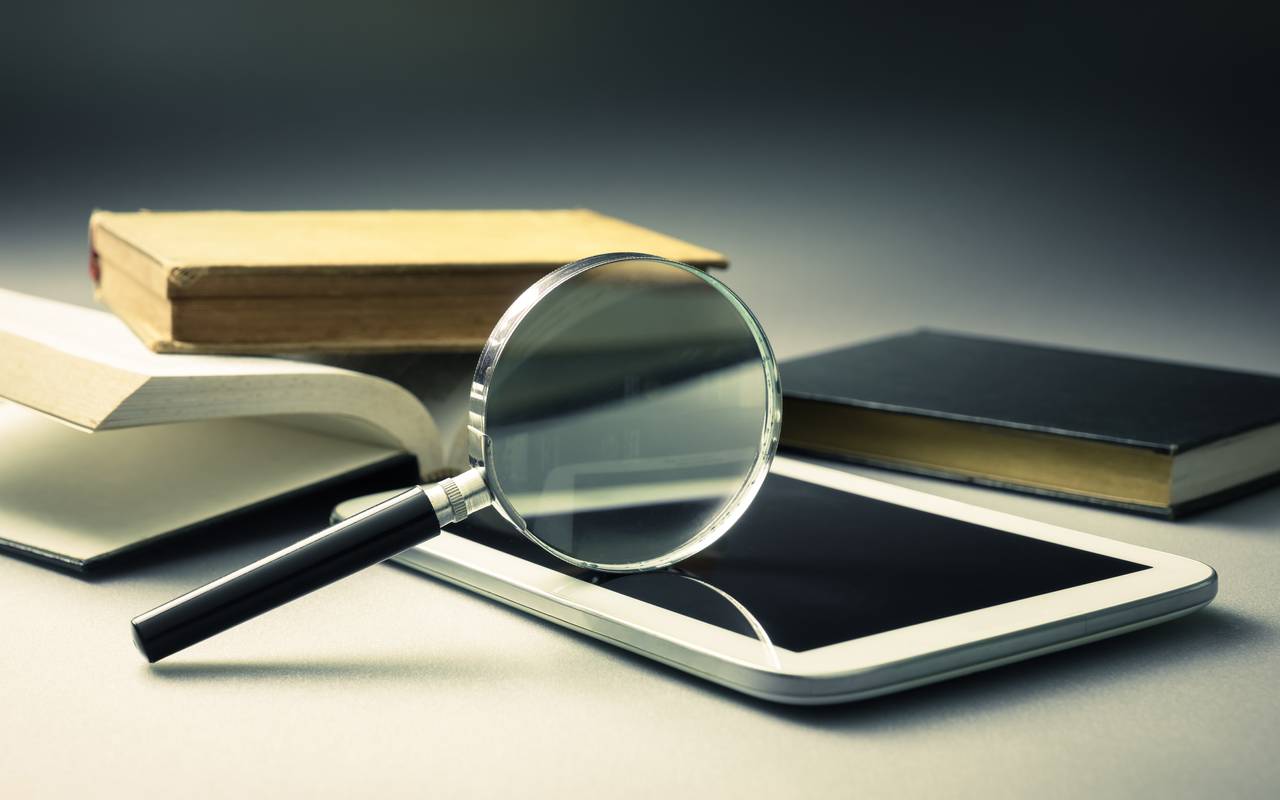 Eine Lupe liegt auf einem Handy. Auch Bücher sind zu erkennen.