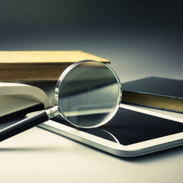 Eine Lupe liegt auf einem Handy. Auch Bücher sind zu erkennen.