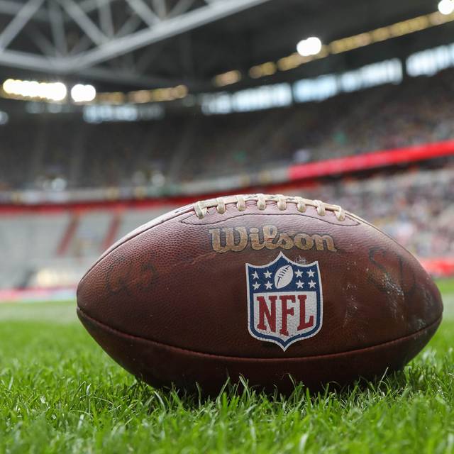 Im Vordergrund ist ein NFL-Football, er liegt auf der Wiese in einem Stadion.