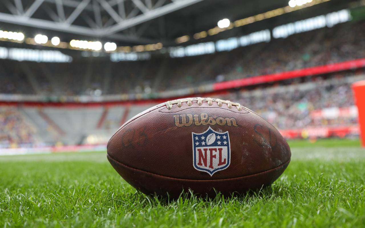 Im Vordergrund ist ein NFL-Football, er liegt auf der Wiese in einem Stadion.