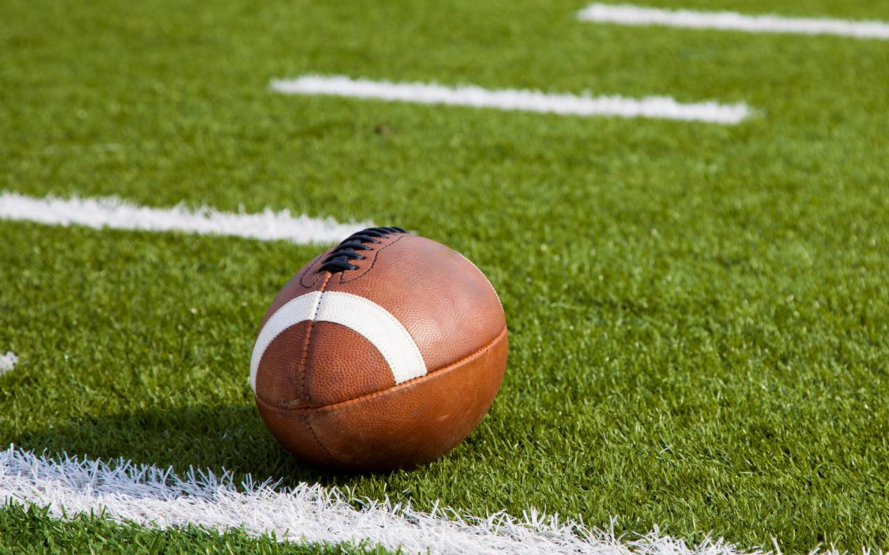 Im Vordergrund ist ein Football, er liegt auf der Wiese in einem Stadion.
