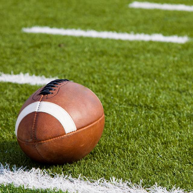 Im Vordergrund ist ein Football, er liegt auf der Wiese in einem Stadion.
