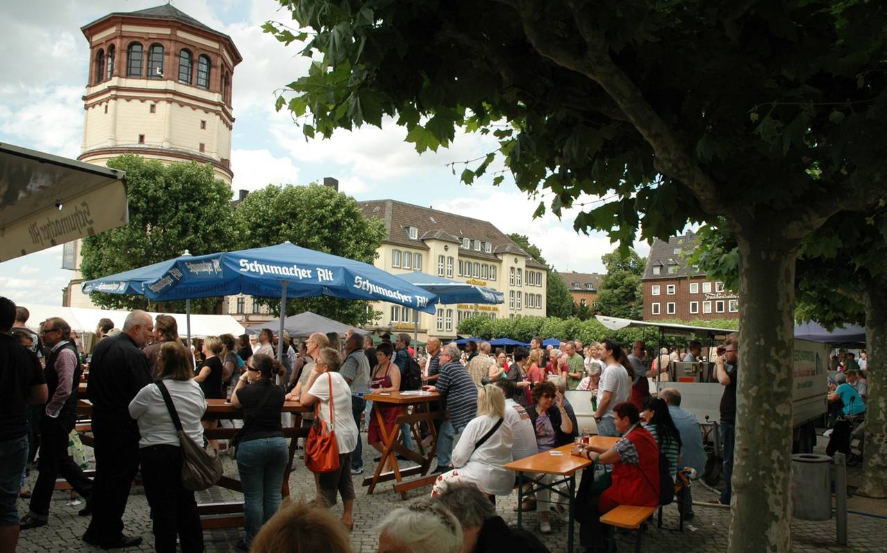 Menschen sitzen auf dem Burgplatz in Düsseldorf an Tischen.