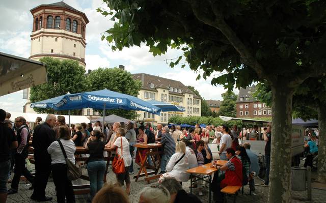 Menschen sitzen auf dem Burgplatz in Düsseldorf an Tischen.