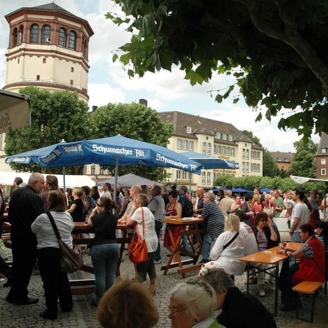 Menschen sitzen auf dem Burgplatz in Düsseldorf an Tischen.