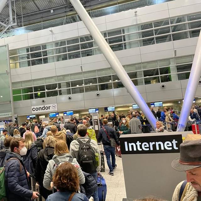 Menschen stehen am Flughafen Düsseldorf in einer langen Warteschlange.