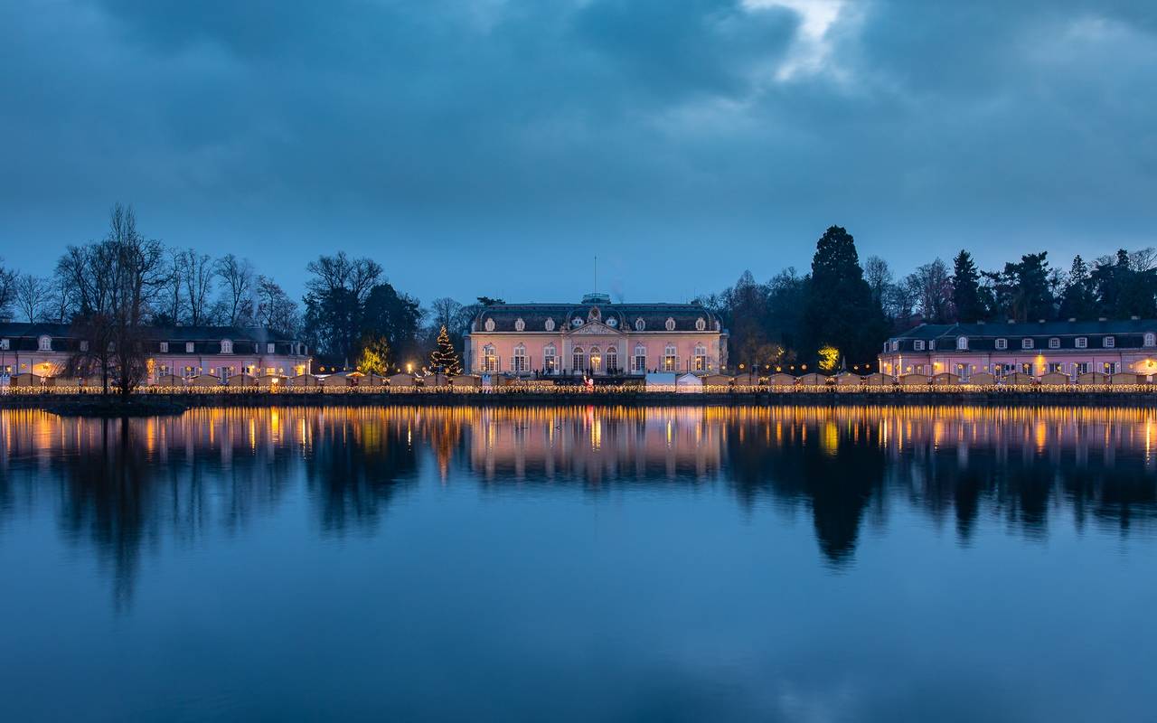 Stadtteil-Weihnachtsmärkte: Ein Weitblick auf den Weihnachtsmarkt vor dem Benrather Schloss. Es dämmert und die Buden sind festlich beleuchtet.