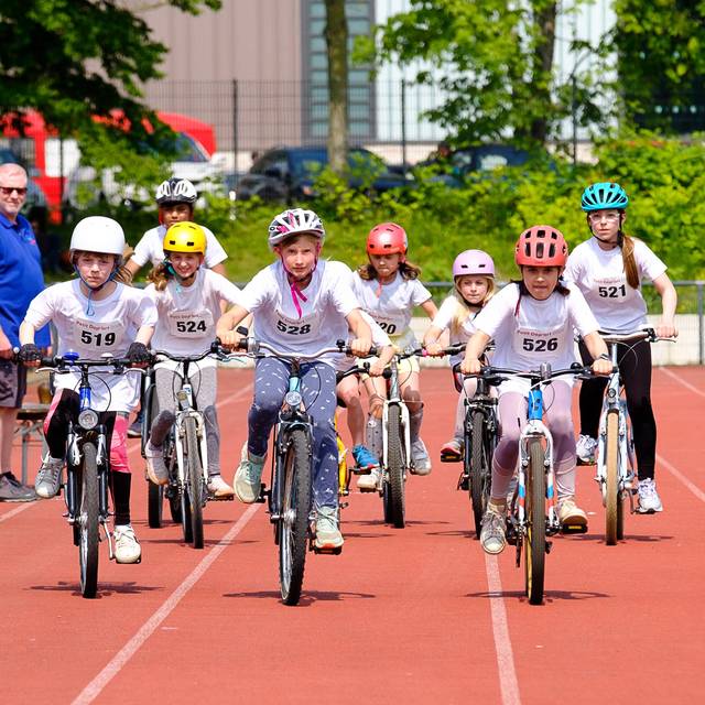 Kinder fahren mit Fahrrädern auf einer Laufbahn. Das Bild zeigt ein Rennen des Wettbewerbs Petit départ.