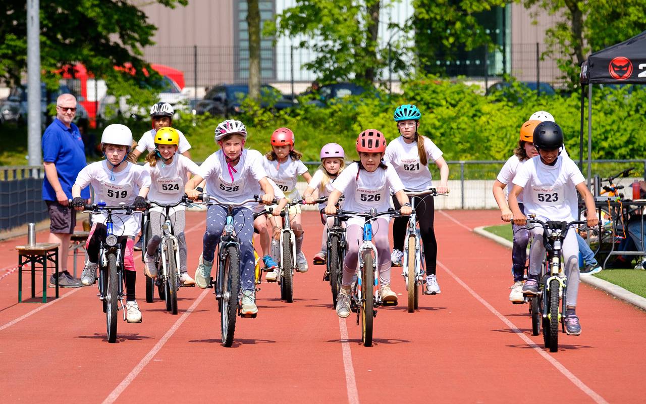 Kinder fahren mit Fahrrädern auf einer Laufbahn. Das Bild zeigt ein Rennen des Wettbewerbs Petit départ.