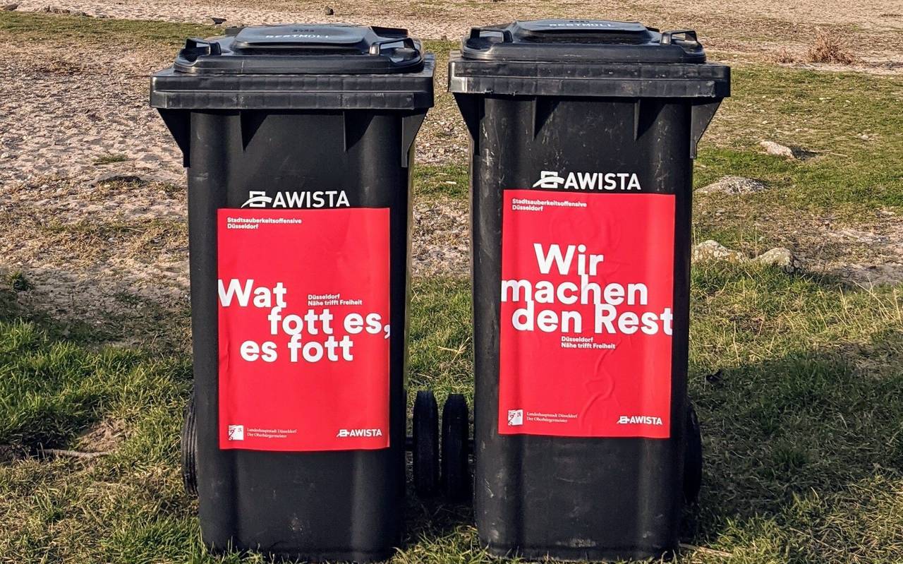 Zwei Mülltonnen, im Hintergrund ist Sand und Rasen zu sehen.