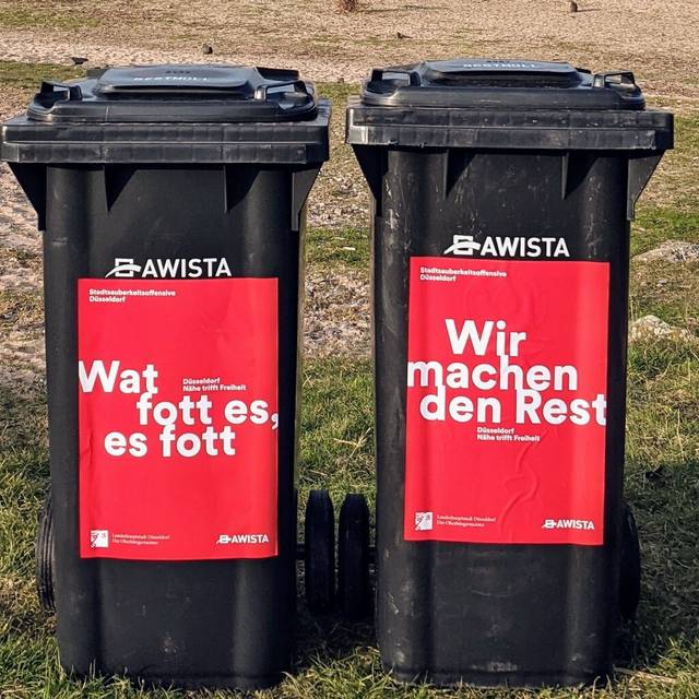 Zwei Mülltonnen, im Hintergrund ist Sand und Rasen zu sehen.