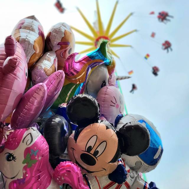 Zu sehen sind bunte Ballons. Im Hintergrund ist ein Fahrgeschäft der Osterkirmes auf dem Staufenplatz.