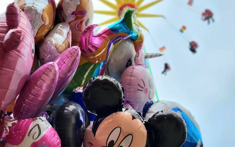 Zu sehen sind bunte Ballons. Im Hintergrund ist ein Fahrgeschäft der Osterkirmes auf dem Staufenplatz.