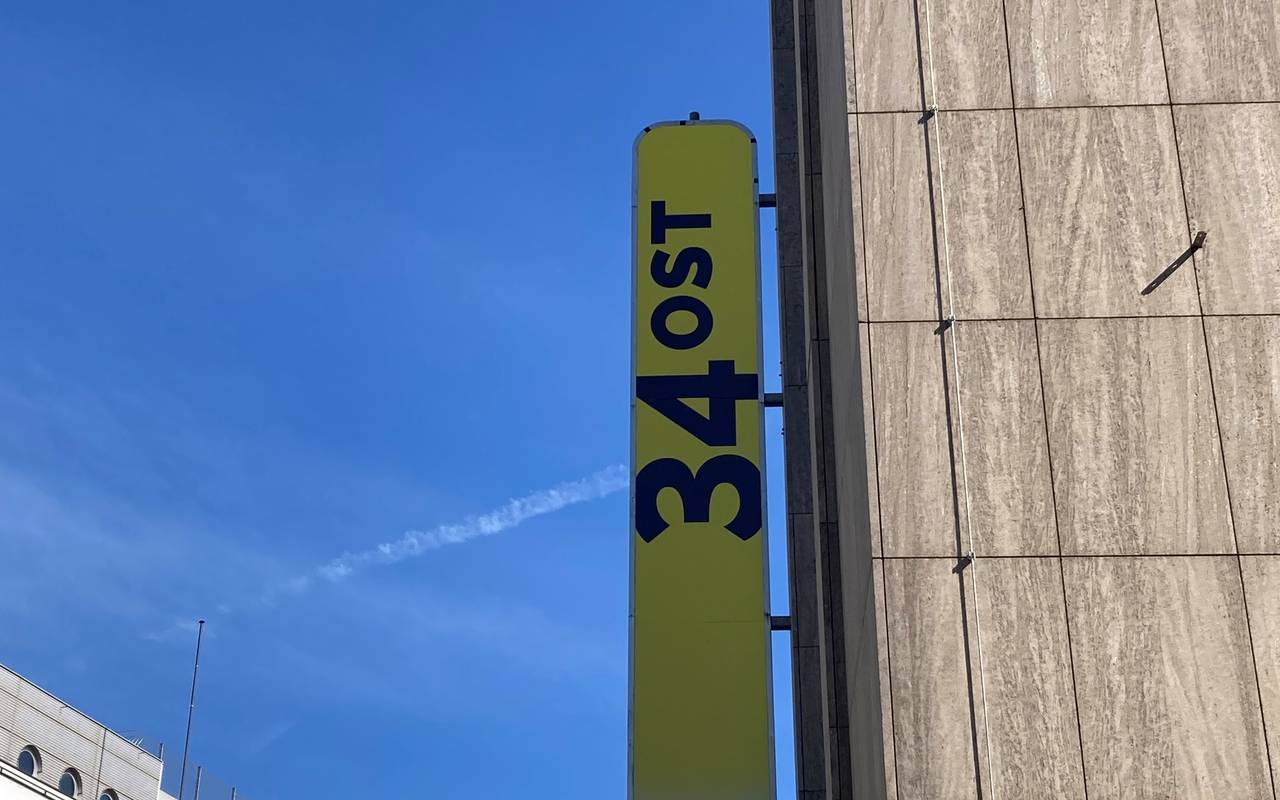 Ein gelbes Schild hängt draußen an einem grauen Gebäude. Darauf steht "34Ost".