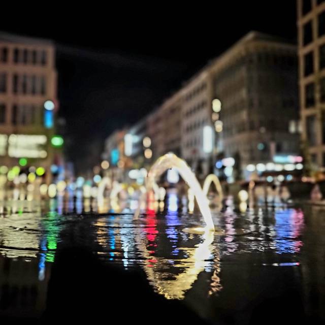 Sprudelnder Brunnen auf der Schadowstraße. Die Einkaufsstraße ist im Hintergrund in der Dunkelheit beleuchtet.