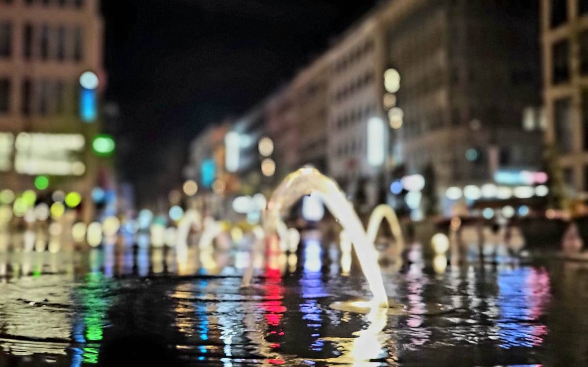 Sprudelnder Brunnen auf der Schadowstraße. Die Einkaufsstraße ist im Hintergrund in der Dunkelheit beleuchtet.
