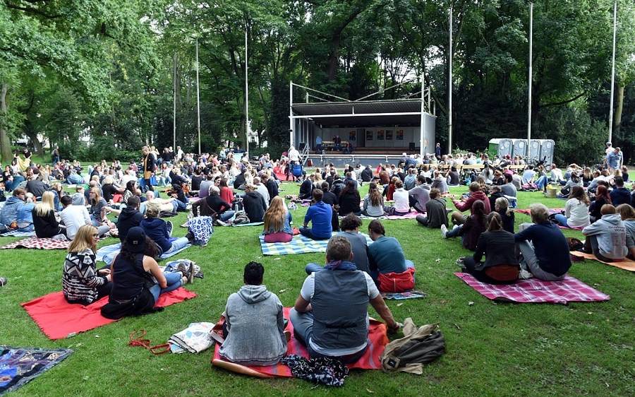 Poetryslam im Hofgarten. Menschen sitzen vor einer Bühne auf dem Rasen.