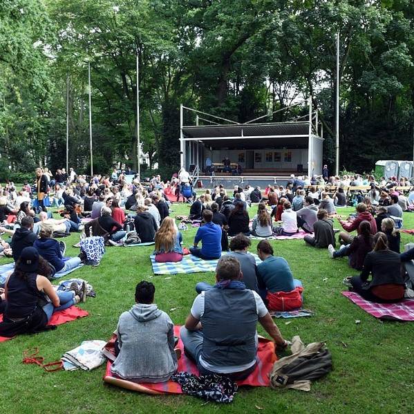 Poetryslam im Hofgarten. Menschen sitzen vor einer Bühne auf dem Rasen.