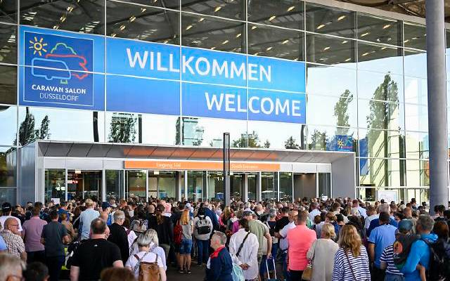 Willkommens-Schild zum Caravan Salon in Düsseldorf. Darunter sind viele Besucher zu sehen.
