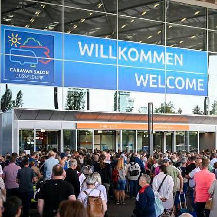 Willkommens-Schild zum Caravan Salon in Düsseldorf. Darunter sind viele Besucher zu sehen.