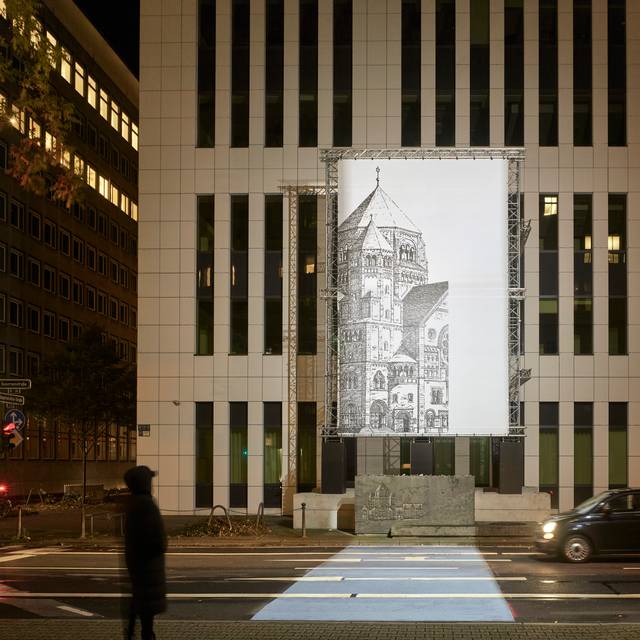 Die Lichtinstallation "missing link_" des Konzeptkünstlers Mischa Kuball. Zu sehen ist eine schwarz-weiß-Abbildung eines Teils der historischen Synagoge auf einer beleuchteten Glasplatte an einer modernen Gebäudefassade.