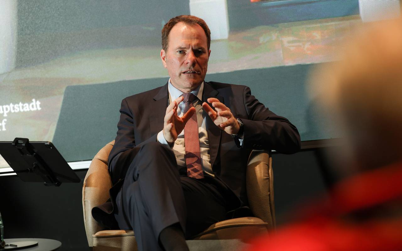 Oberbürgermeister Stephan Keller sitzt auf einem Podium und redet.