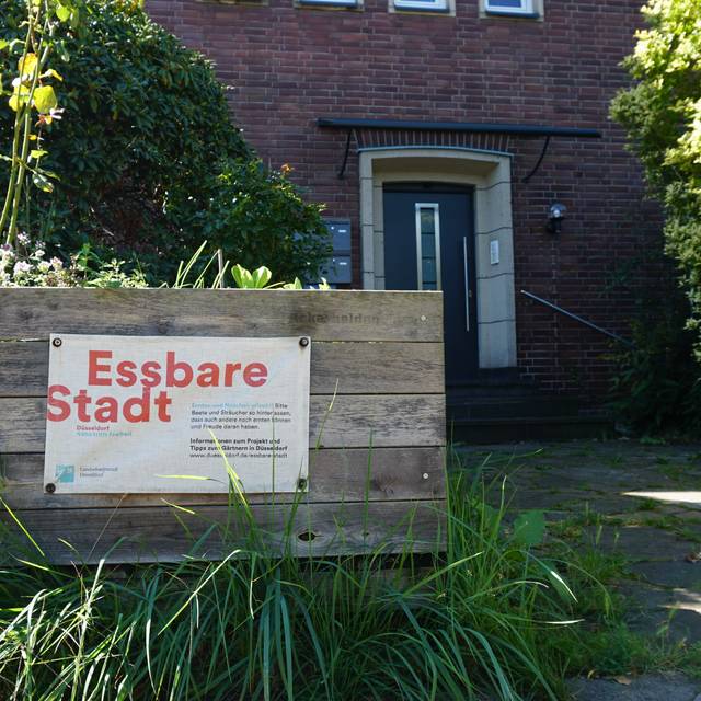 Blick auf ein Hochbeet der Stadt vor einem Wohnhhaus. Auf dem Hochbeet ist ein Papier mit dem Aufdruck "Essbare Stadt"