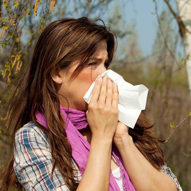 Eine Frau schnäuzt in ein Taschentuch. Sie hat Schnupfen, bzw. auch eine Allergie.