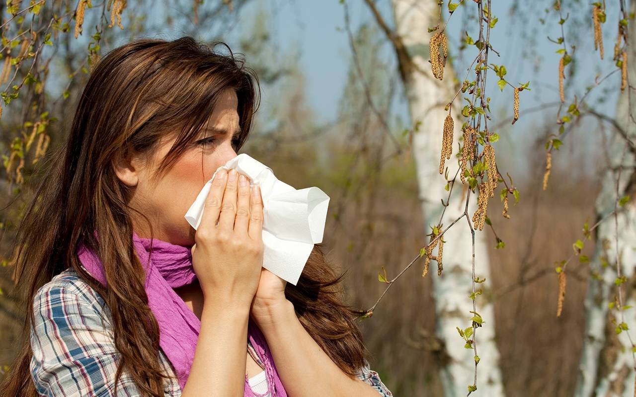 Eine Frau schnäuzt in ein Taschentuch. Sie hat Schnupfen, bzw. auch eine Allergie.
