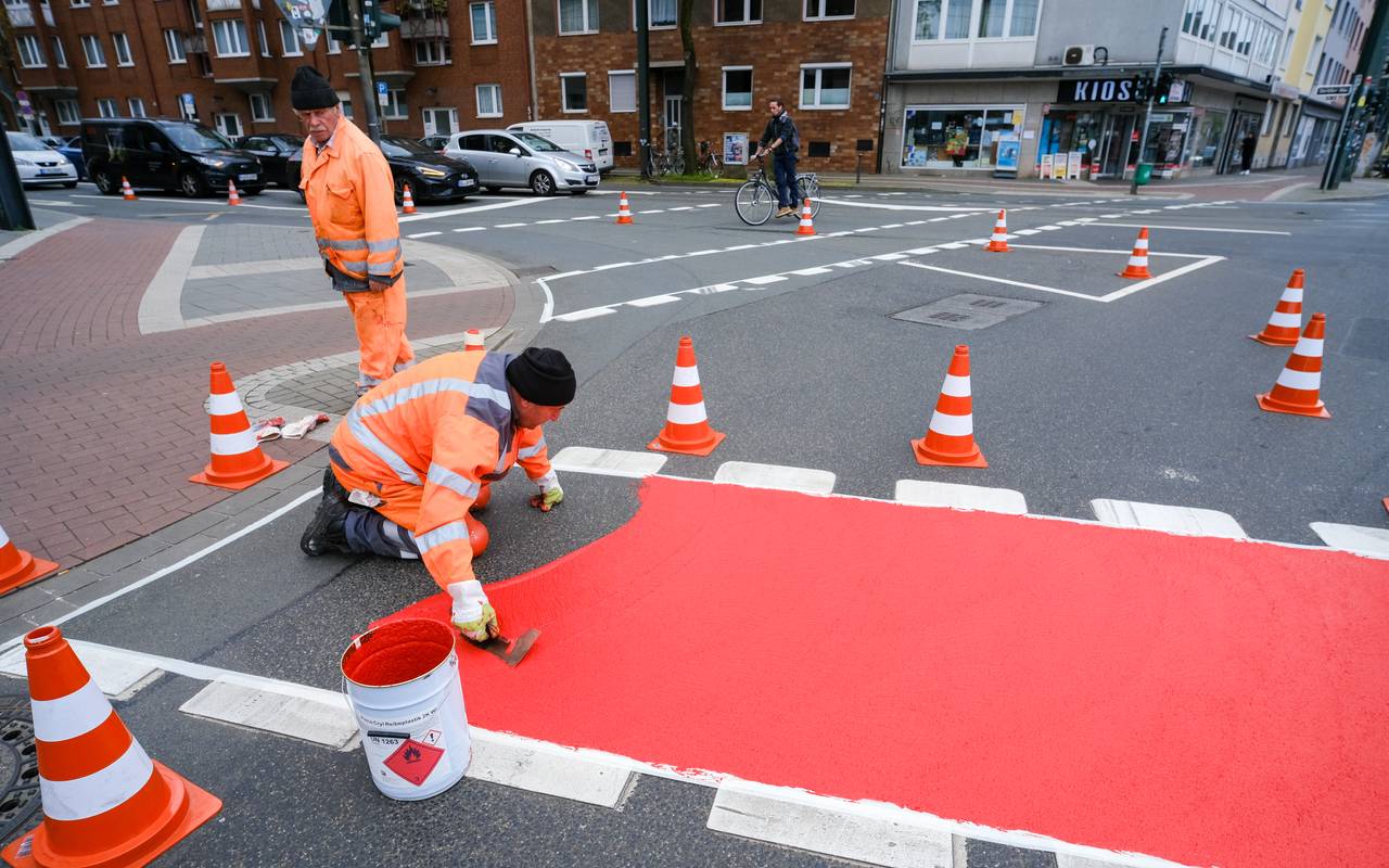 Ein Radweg wird rot markiert, zwei Bauarbeiter bei der Arbeit