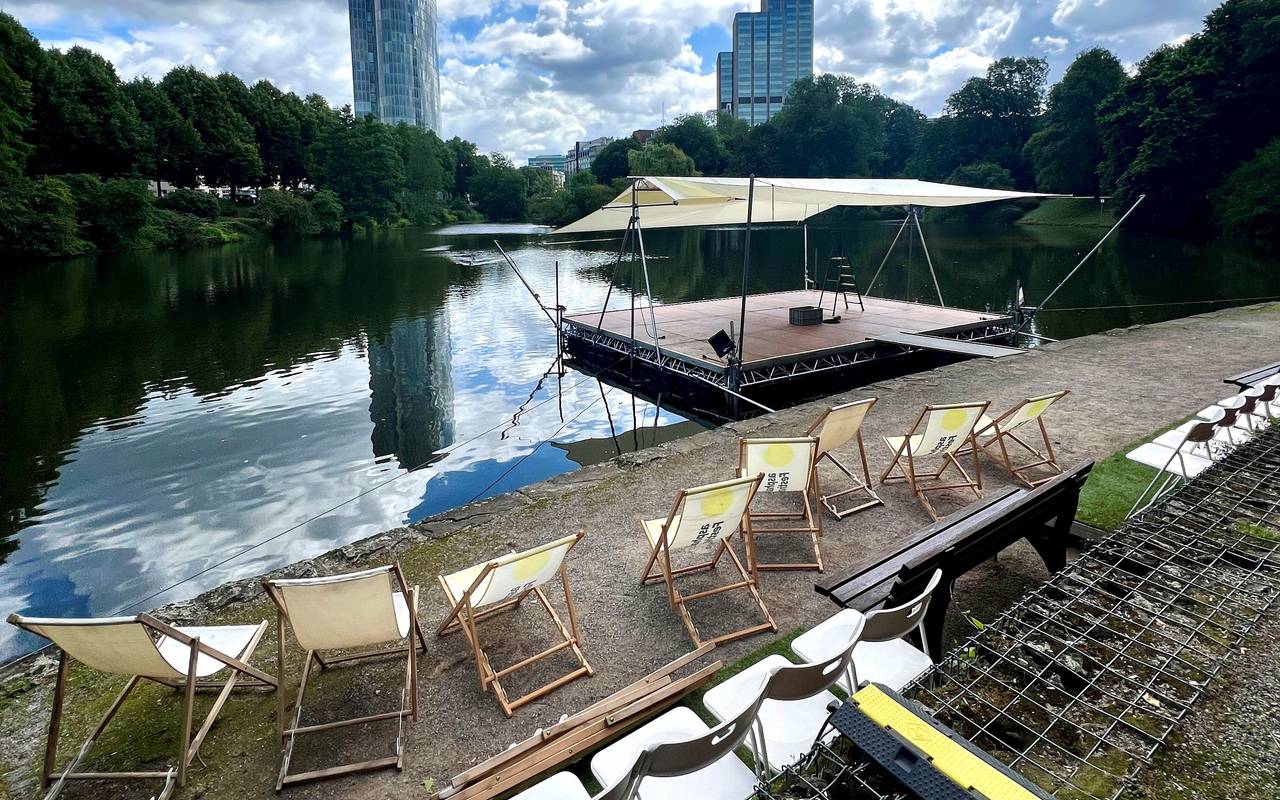 Eine Aufnahme von der Seebühne am Schwanenspiegel. Stühle stehen am Rand des Schwanenspiegels. Im Hintergrund sind Hochhäuser.