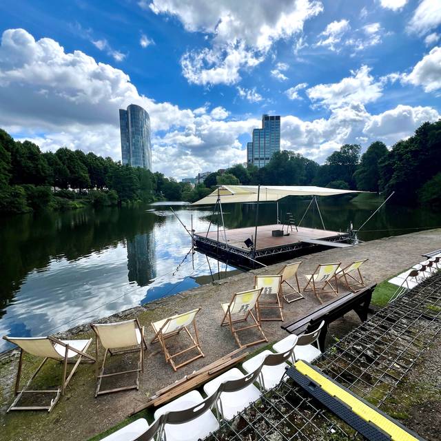 Eine Aufnahme von der Seebühne am Schwanenspiegel. Stühle stehen am Rand des Schwanenspiegels. Im Hintergrund sind Hochhäuser.