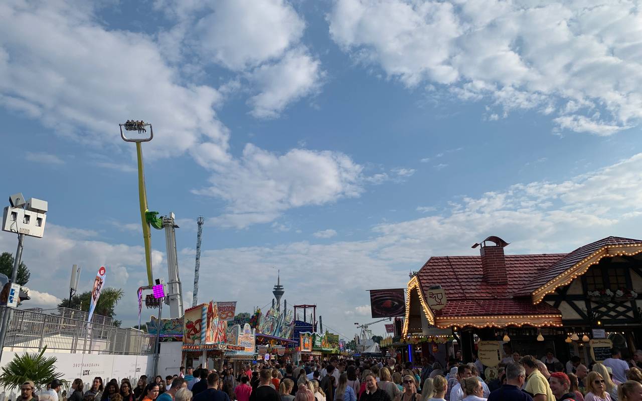 Die Rheinkirmes bei schönem Wetter. Viele Menschen schlendern über den Platz und an den Fahrgeschäften vorbei.