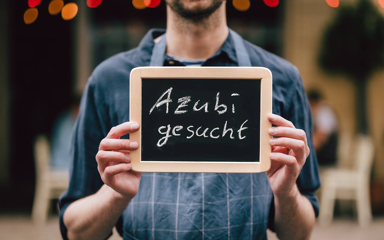 Ein Mann hält ein Schild mit der Aufschrift "Azubi gesucht".