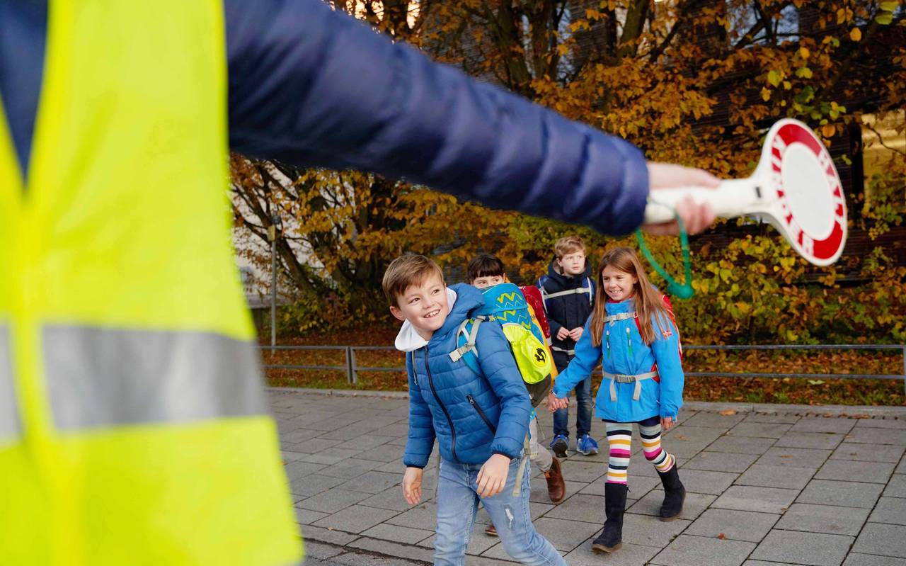I-Dötzchen auf ihrem Schulweg. Ein Ordner regelt mit einer Kelle den Verkehr und sorgt so für Sicherheit.
