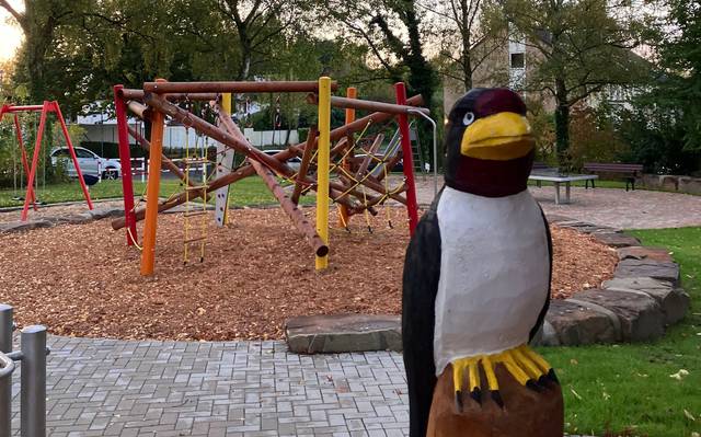 Eine Holzschwalbe auf einem Spielplatz in Düsseldorf Unterbach. Zu sehen ist auch ein Spielgerüst und Sand.