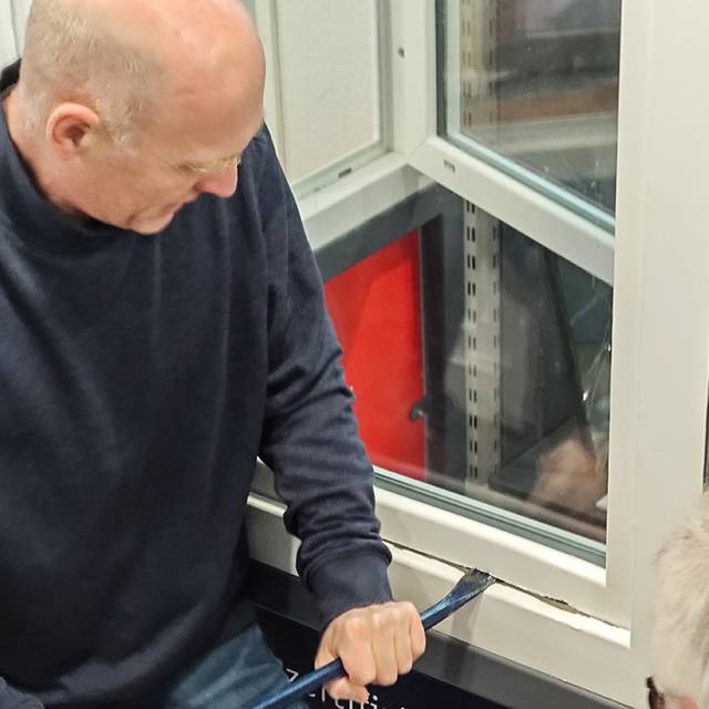 Ein Polizist demonstriert mit Einbruchswerkzeug, wie eingebrochen wird. Er hebelt ein Fenster auf.